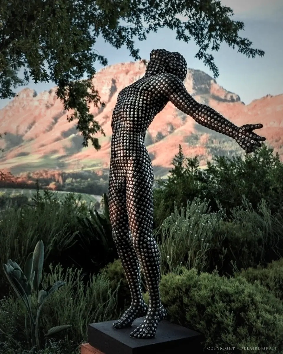 Faith, a life-size sculpture by Anton Smit, arms open towards the mountains at Delaire Graff Estate