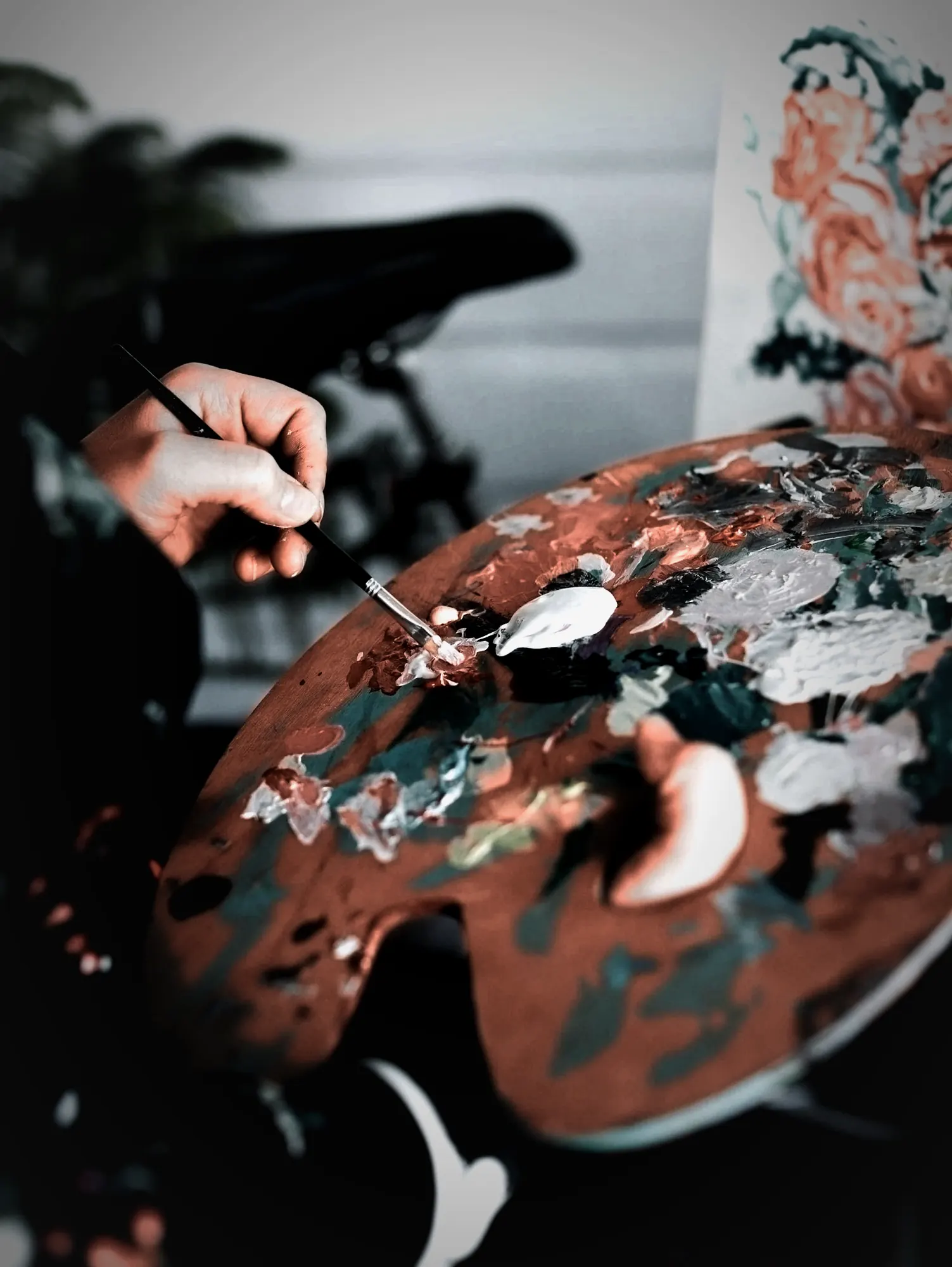 A hand mixing paint on a well-used wooden palette