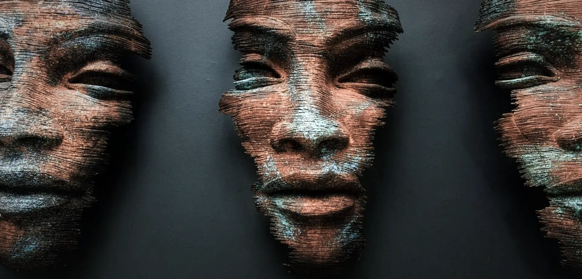 Rusted steel masks of a face with closed eyes, flecked with verdigris, mounted on a dark wall